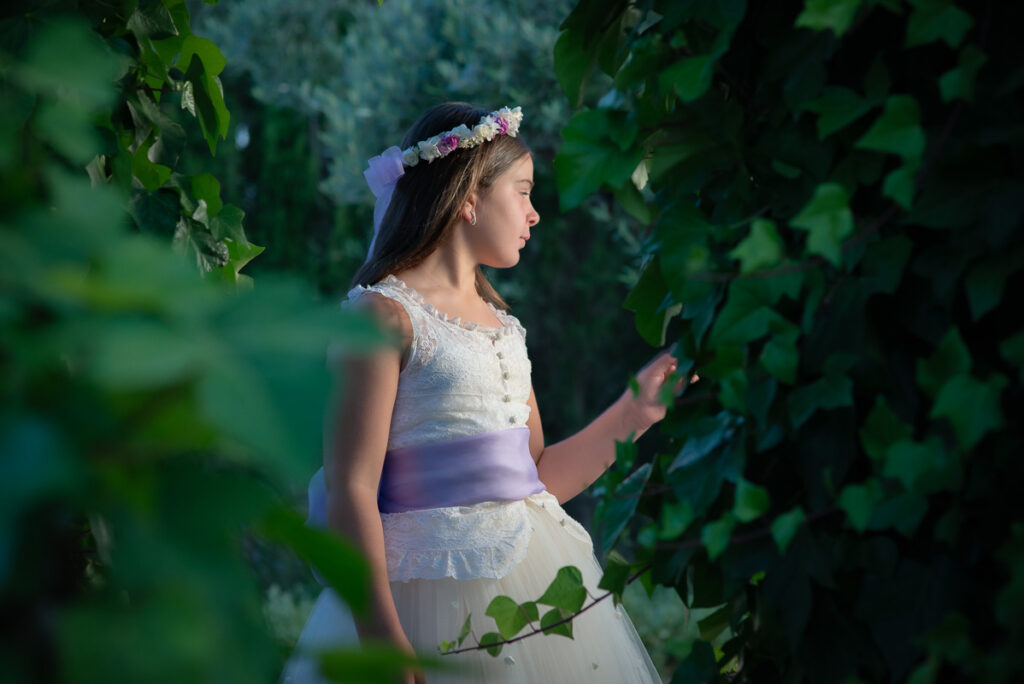 Alexia posa con su vestido blanco y corona de flores durante una sesión de comunión al aire libre.